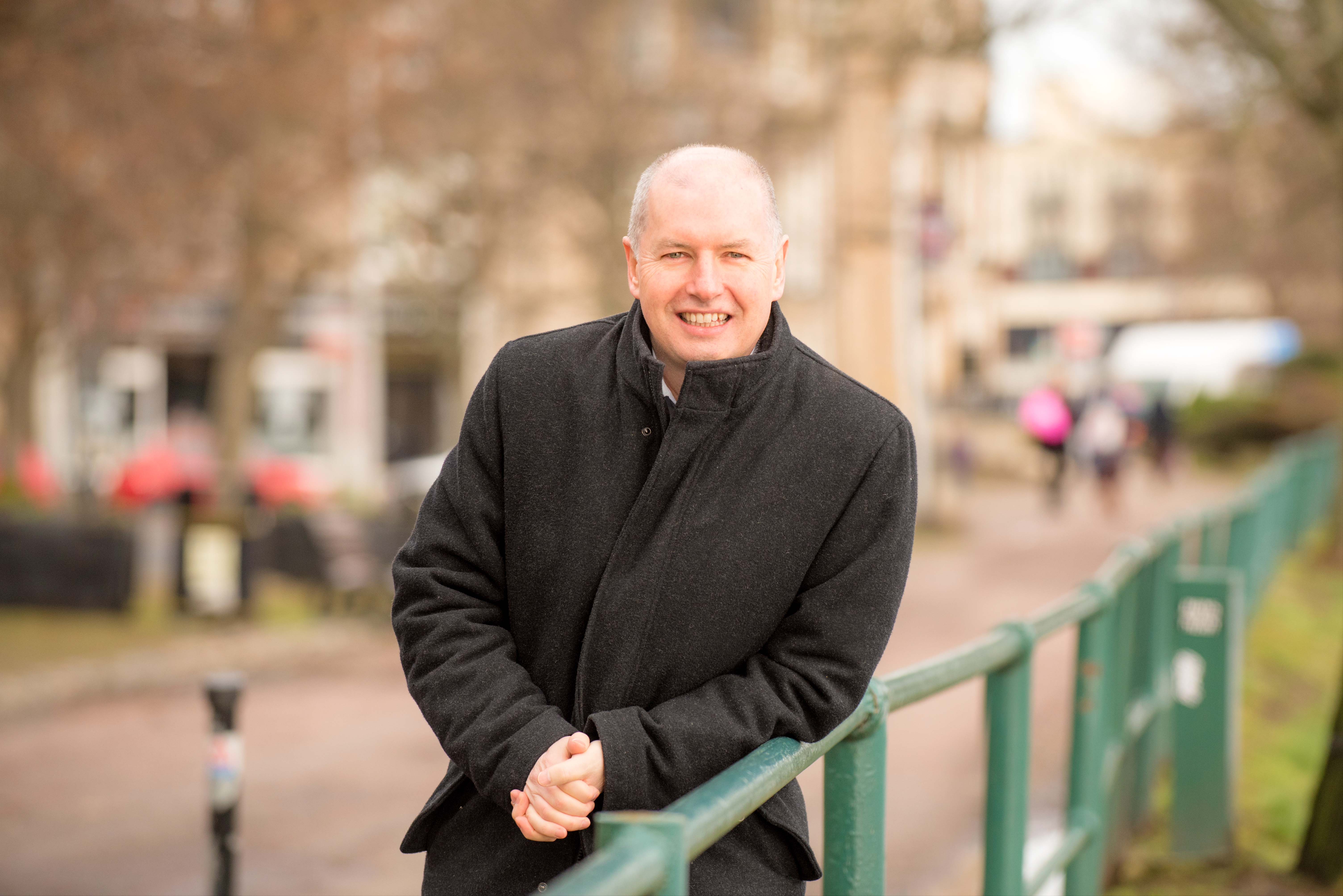 Man smiling leaning against a metal fence